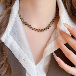 Dettaglio della collana con perle di occhio di tigre e catena d'oro indossata su camicia