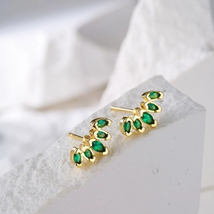 Macro detail of geometric 18K gold plated earrings with emerald zircon leaf design