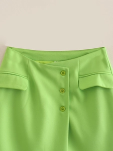 Detail of lime green high-waisted skirt featuring asymmetric buttons and flap pockets