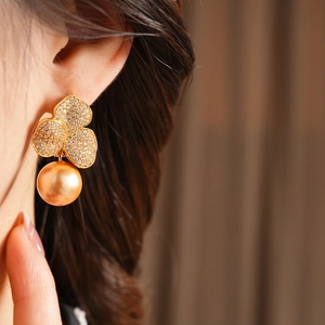 Macro side view of a gold-plated flower earring with zircons and a large gold pearl