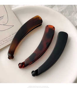 Three elegant matte banana hair clips in amber and black on a white ceramic plate