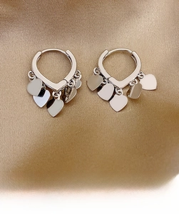 Close-up of silver heart fringe hoop earrings on elegant golden silk background