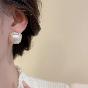 Macro detail of elegant square pearl earring with gold textured frame on model