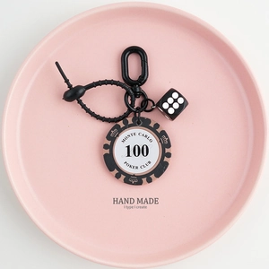Detail of black poker chip keychain with dice and silicone strap on pink ceramic tray