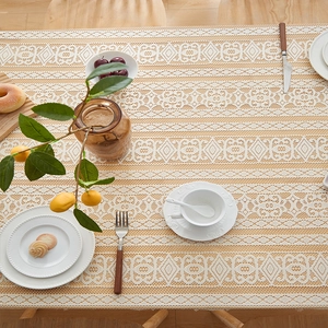 Detail of beige lace tablecloth with hollow geometric patterns on wooden dining table