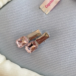 Detail of two silver metal hair clips featuring square pink rhinestones on ribbed fabric