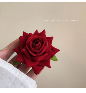 Detail of red velvet rose hairpin with green leaves held in hand for close-up view