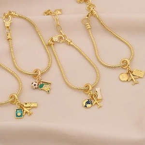 Golden snake chain bracelets with travel charms like airplanes and globes on beige fabric