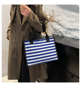 Dettaglio della grande borsa tote in tela a righe con manico nero e chiusura a scatto