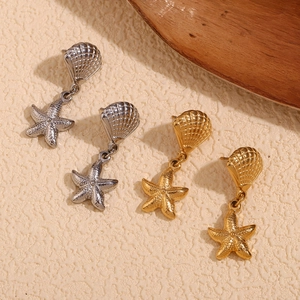 Macro shot of 18K gold and silver starfish and shell earrings on natural stone surface