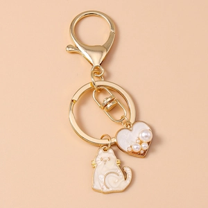 Detailed view of golden metal keychain with white enamel cat and pearl heart pendant