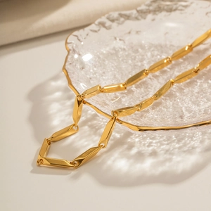 Close-up of golden geometric link necklace with polished finish in glass dish