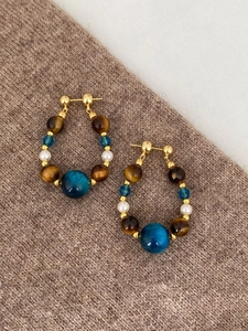 Détail de boucles d'oreilles en perles, oeil de tigre et breloques bleues sur tissu
