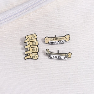 Three creative medical enamel pins with puns like I'VE GOT YOUR BACK on beige canvas