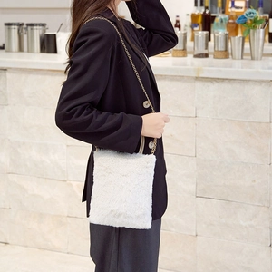 White faux fur crossbody bag with gold metal chain strap shown on modern indoor model
