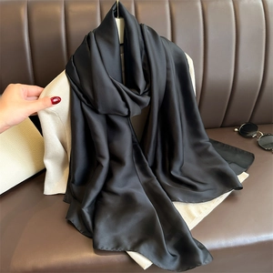 Detail of soft black satin long scarf styled elegantly on a brown leather sofa