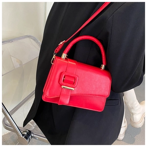 Close-up of bright red leather crossbody bag with square buckle on black blazer