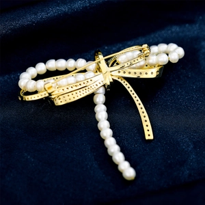 Detail of a golden bow brooch with micro-pave zircons and white pearl tassels