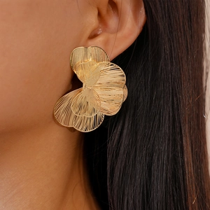 Close-up of model wearing gold layered flower earrings with hollow metal texture