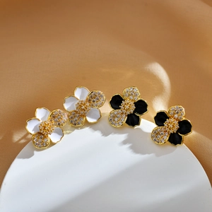 Detail of flower stud earrings in white and black enamel with gold borders and crystals