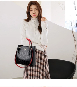 Detail of elegant black leather tote with red straps and embossed brand logo on front