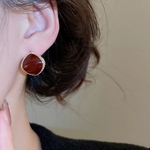 Macro shot of red zircon stud earring with gold plating and pavé white diamonds on ear