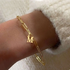 Elegant gold paperclip chain bracelet with a letter M pendant worn on a wrist