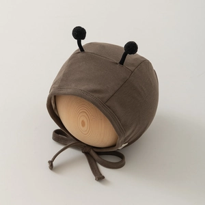 Close-up of brown knit baby bonnet with cute black antenna-like pompoms and ties