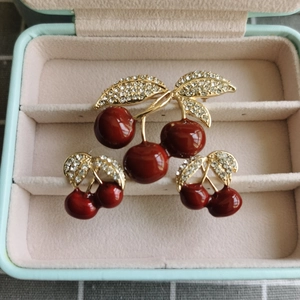 Détail de la broche cerise en émail rouge et boucles d'oreilles avec feuilles dorées