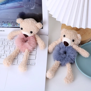 Detail showing plush teddy bear hair ties in pink and grey-blue on a clean desk background