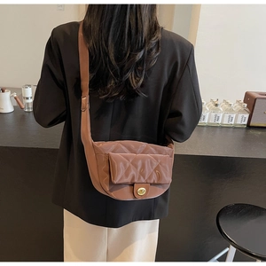 Detailed view of brown quilted nylon saddle bag with gold clasp worn as a crossbody