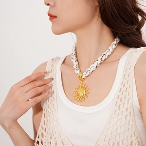 Detail view of a gold sun pendant on white braided rope, bohemian style on model