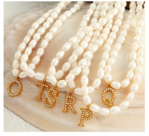 Close-up of pearl necklaces with gold initial letter pendants on mother of pearl base