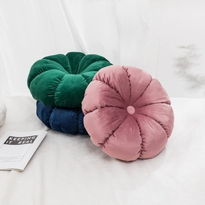 Modern velvet pumpkin cushions in pink, green and blue stacked on a white bed