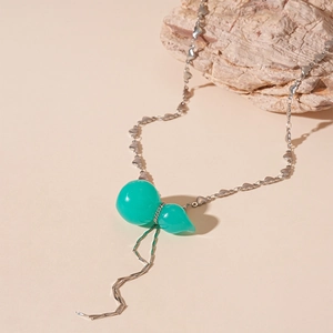 Détail du pendentif gourde vert émeraude et collier chaîne à cœurs sur fond de pierre neutre