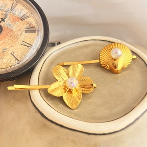 Gold hair clip set with shell and flower designs featuring pearls on a ceramic dish