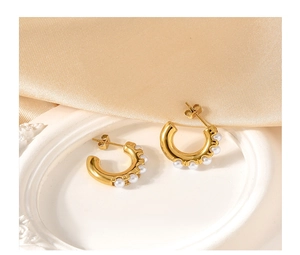 Close-up of gold C-shape earrings with inlaid white pearls on elegant satin fabric
