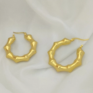 Detailed view of golden bamboo-style hoop earrings on elegant white silk background