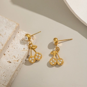 Close-up of gold cherry earrings with sparkling crystals on a textured stone surface