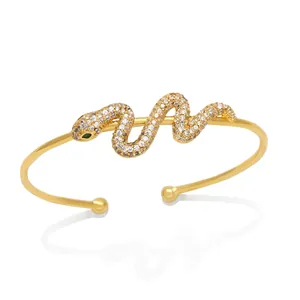 Elegant gold snake open bangle with white zircons and green gemstone eyes on white background