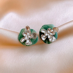 Close-up of green marble resin earrings with silver flower detail on beige silk