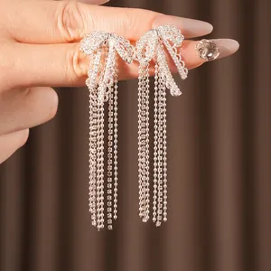 Silver bow tassel earrings with sparkling cubic zirconia on a minimalist hand view