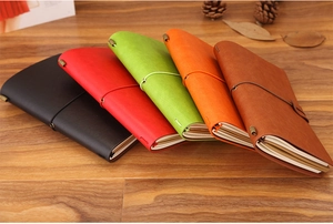 Stack of vintage leather traveler notebooks in five colors on a rustic wooden desk