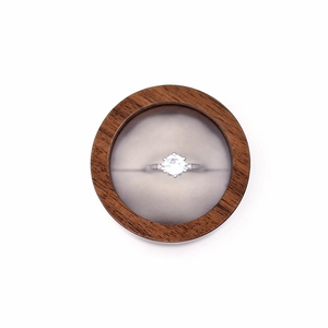 Close-up of a silver diamond ring presented inside a round minimalist wooden jewelry box