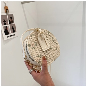 Detail of round straw bag featuring pink floral embroidery and white leather trim