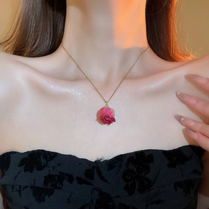 Detail of a delicate gold necklace with a pink dried rose pendant worn by a model