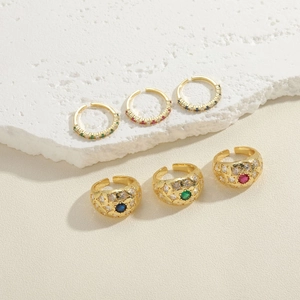 Detailed set of six gold rings with red green blue gems on textured stone surface