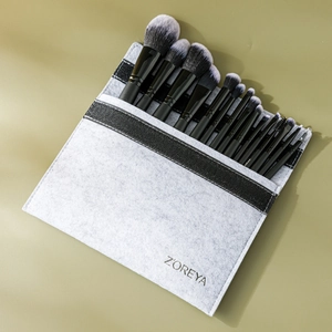 Flat lay of 15-piece black makeup brushes with gradient bristles in a grey felt bag