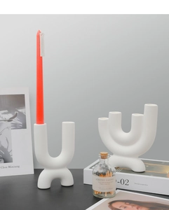 Detail of white matte ceramic U-shaped wavy candle holder set on a black table surface