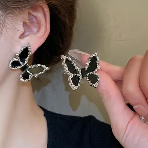 Elegant butterfly stud earrings with black enamel and textured silver-tone frame on model